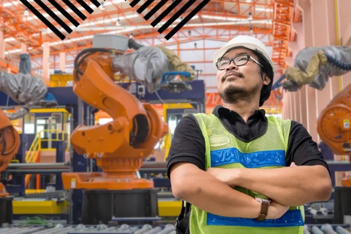 Man standing with three robotic arms behind him in a manufacturing setting